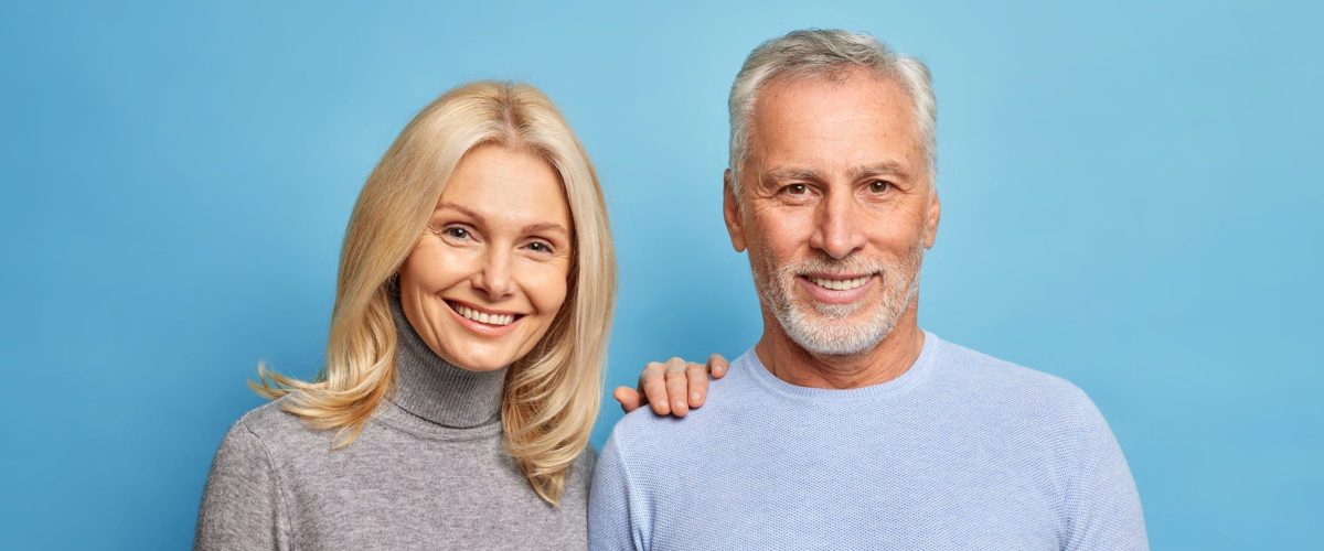 Photo of happy senior woman and man express positive emotions pose together being still in love isolated over blue background. Smiling grandmother grandfather make family photo glad to meet children